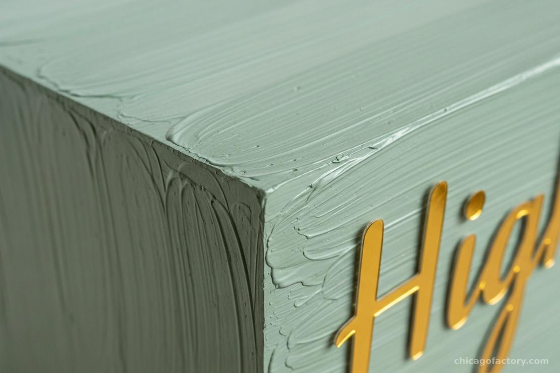 Detail shot of white brushstrokes on the back of a clear acrylic sign with gold text