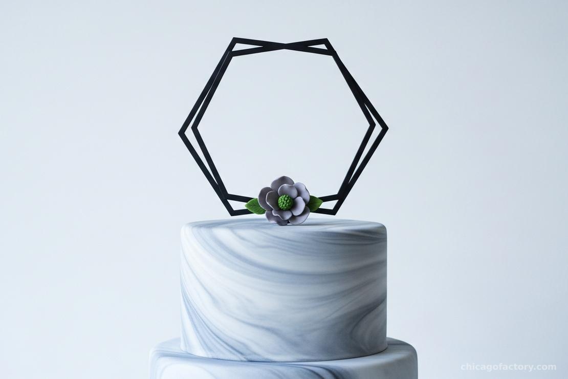 A modern hexagon-shaped cake topper with geometric lines on a grey marble-effect wedding cake.