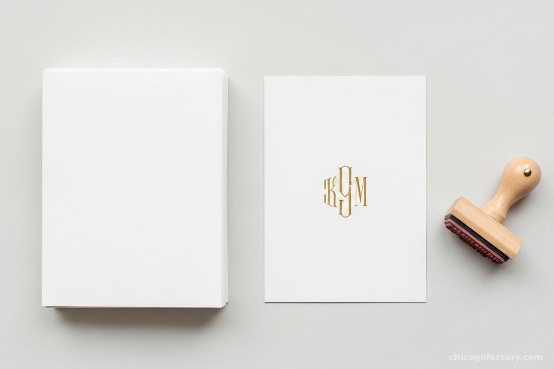 Flat lay of blank folded cards being stamped with a custom monogram in gold ink.