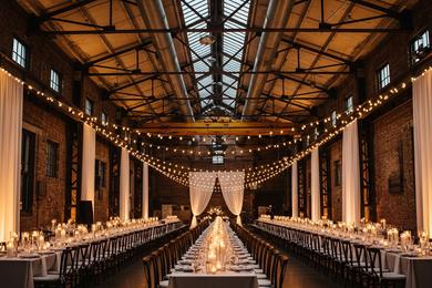 A wide shot of a wedding reception in a warehouse, showing the contrast between rough brick walls and elegant table settings.